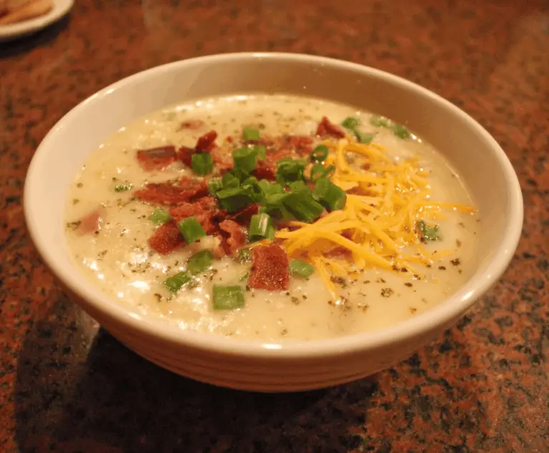 Creamy Outback Steakhouse Potato Soup garnished with chopped green onions, served in a bowl with a rustic background, perfect for a comforting appetizer or starter.