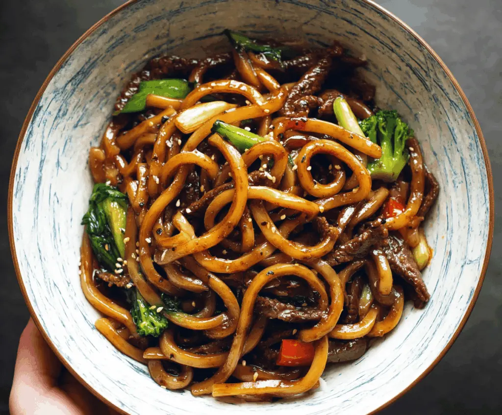Savory Beef Black Pepper Udon noodles garnished with fresh green onions on a white plate