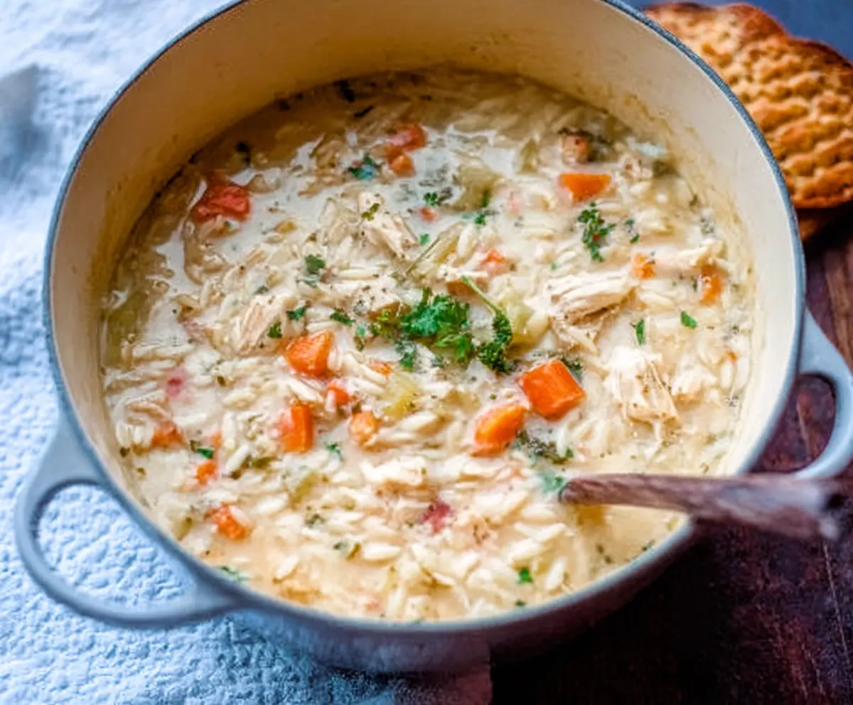A bowl of creamy chicken orzo winter soup garnished with herbs and vegetables.