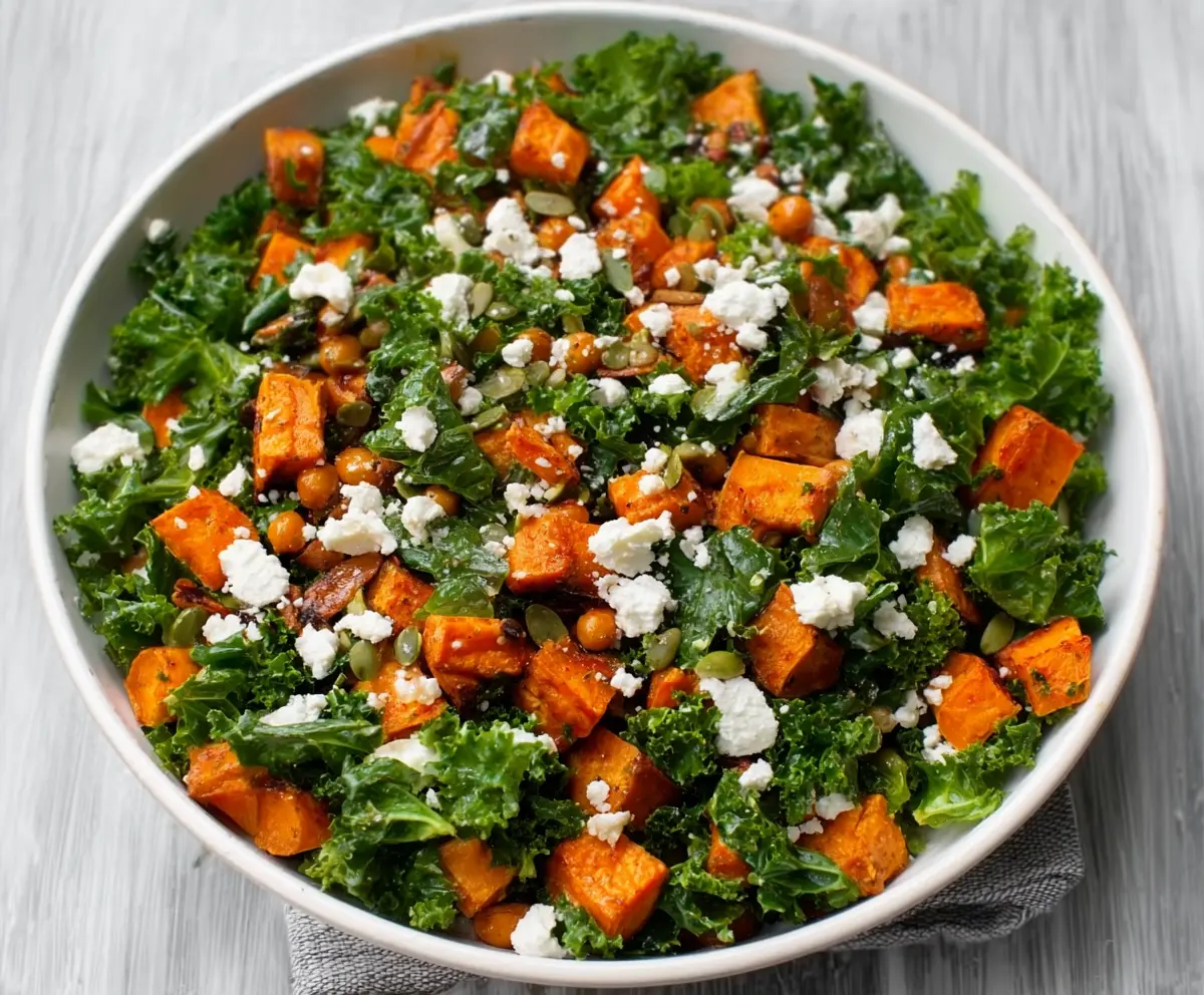 Colorful Kale and roasted sweet potato salad with fresh vegetables on a white plate.