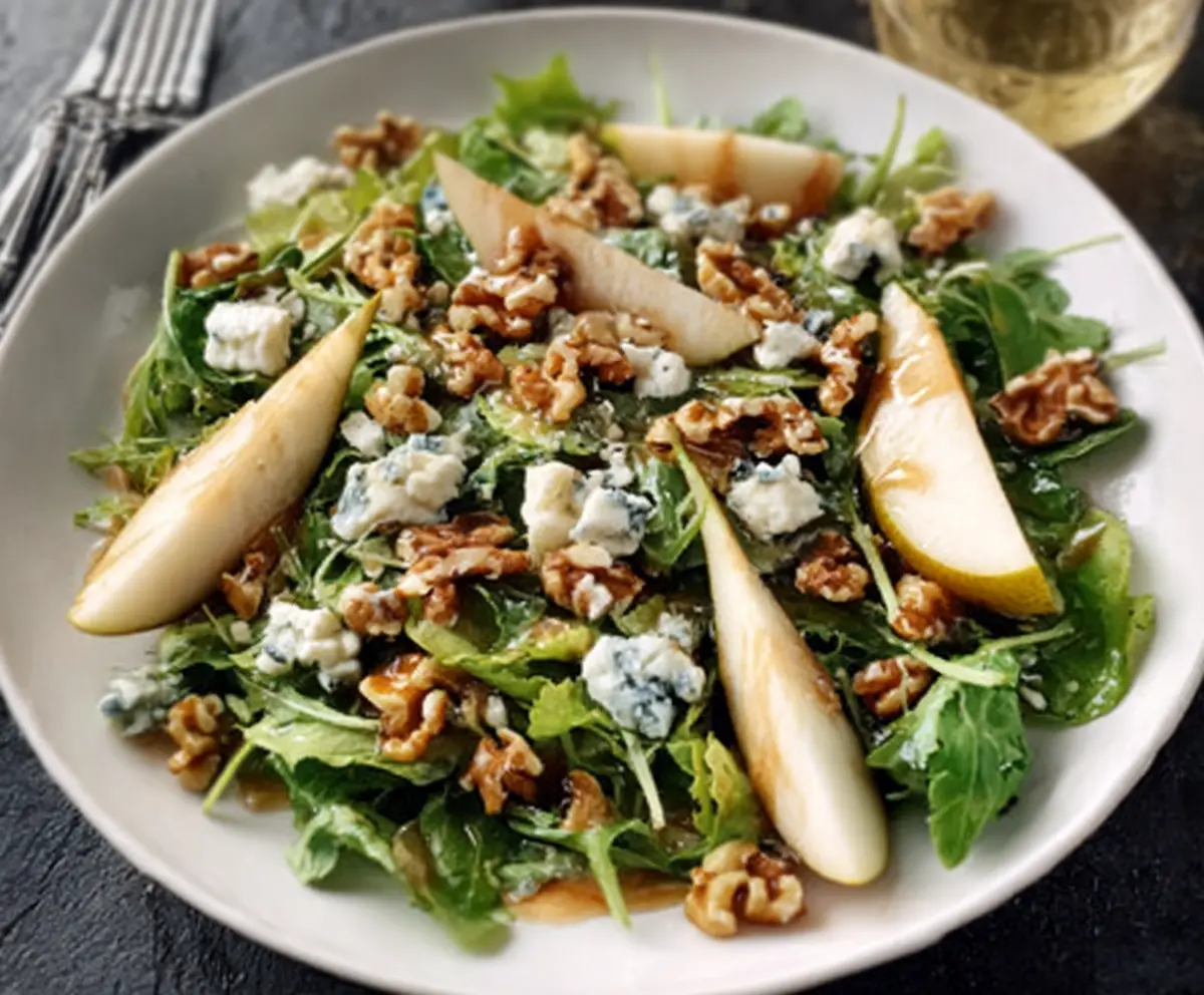 Fresh pear and Gorgonzola salad topped with candied walnuts on a white plate.