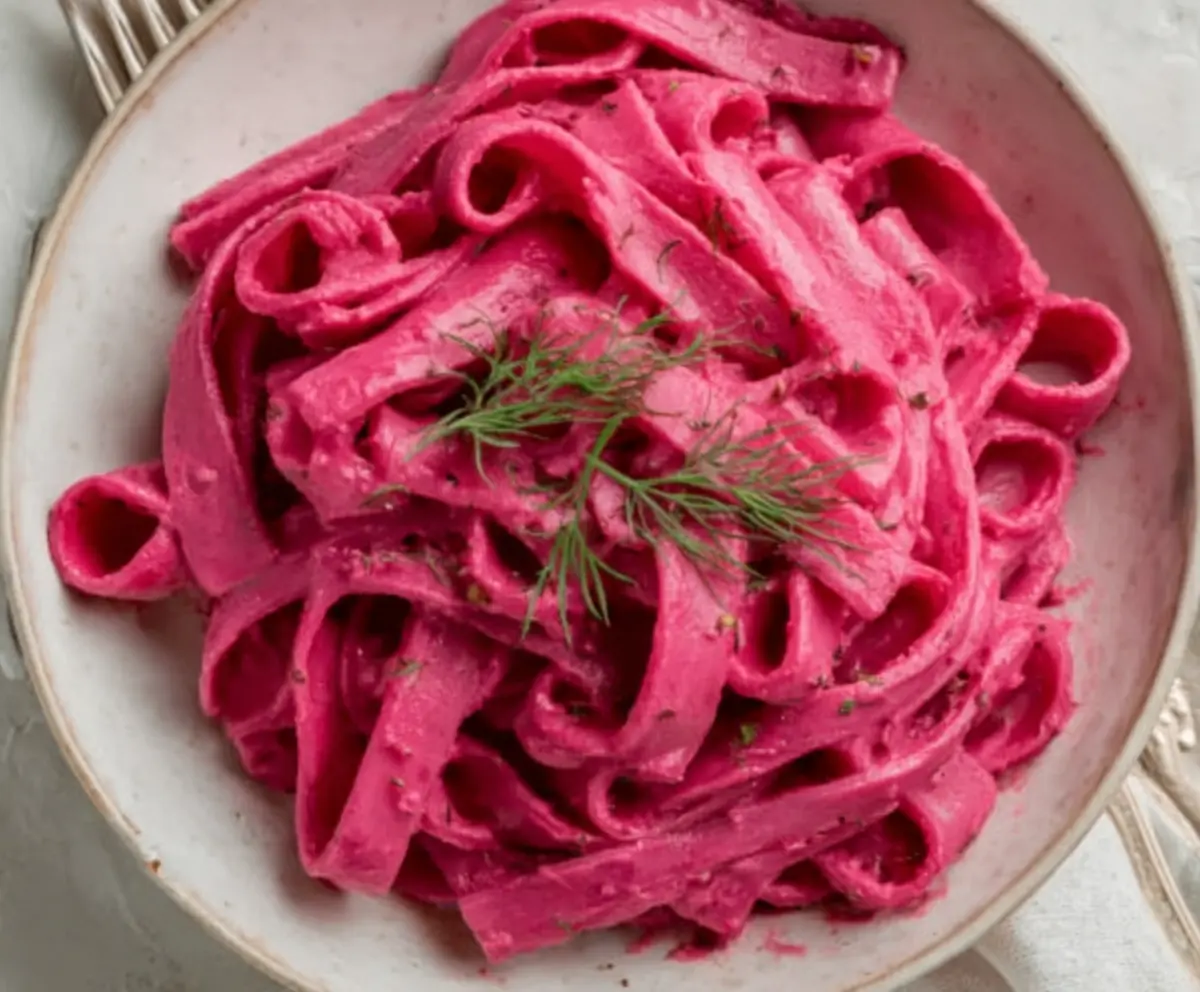 Vibrant pink pasta topped with creamy beet sauce, garnished with fresh herbs for a colorful and delicious vegan meal.