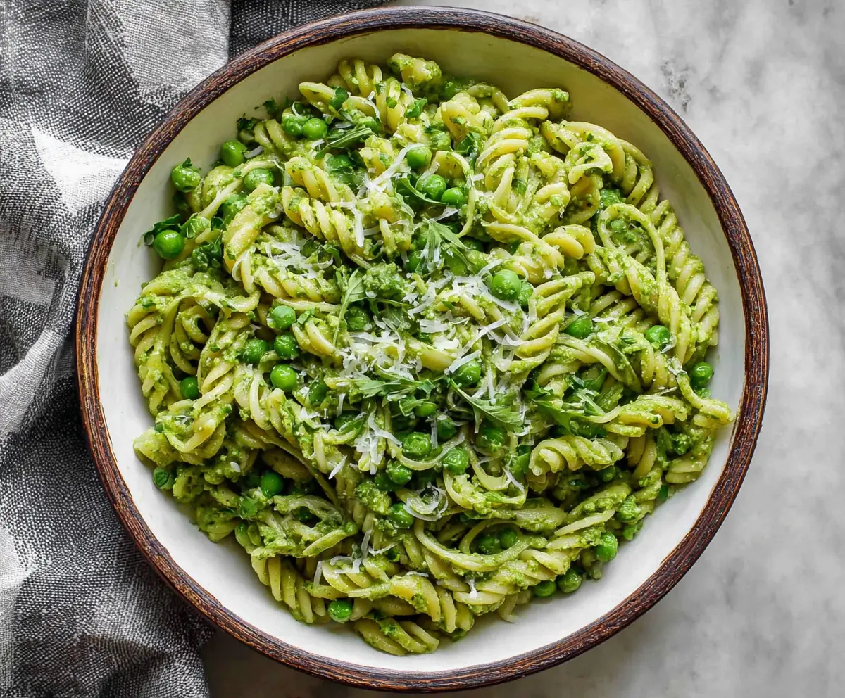 Creamy spring pea pesto pasta garnished with fresh basil and parmesan cheese.
